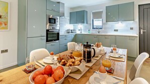 A modern kitchen with light blue cabinets, a dining table set with breakfast items, and a large window. - 2 Bed in Holsworthy (oc-50598) (Sessacott)