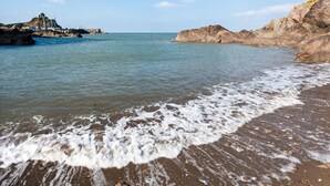 Een strand met rotsformaties, rustig water en een heldere lucht.