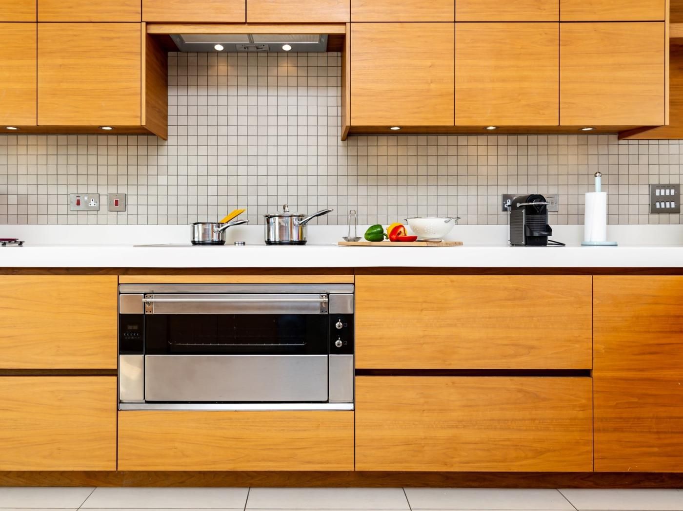 A modern kitchen with wooden cabinets, a stainless steel dishwasher, and a white countertop with various kitchen items.