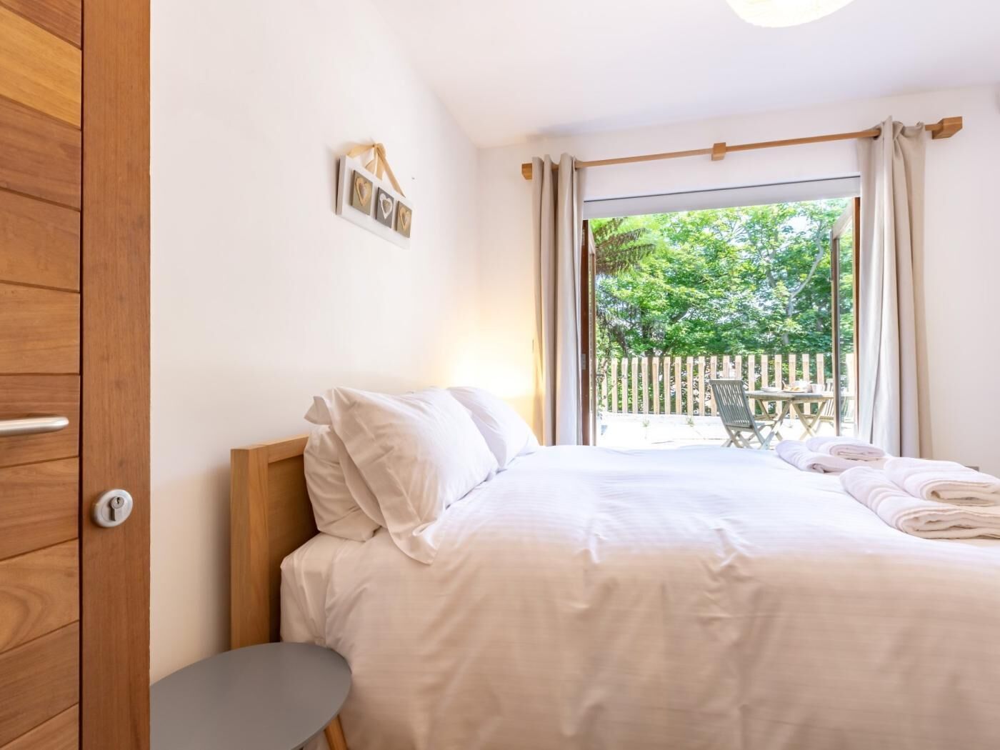 A bedroom with a bed, a wooden wardrobe, a small table, and a view of the outdoors.