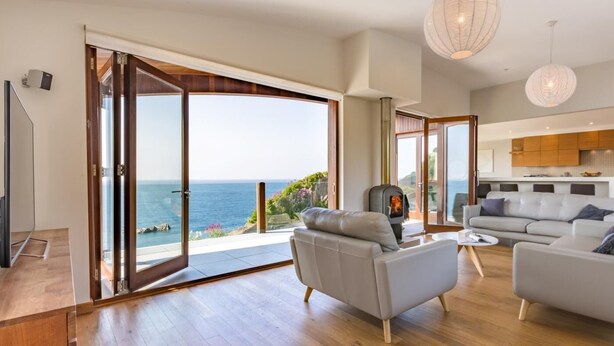 Een ruime woonkamer met een grote schuifpui die uitkomt op een balkon met uitzicht op zee.