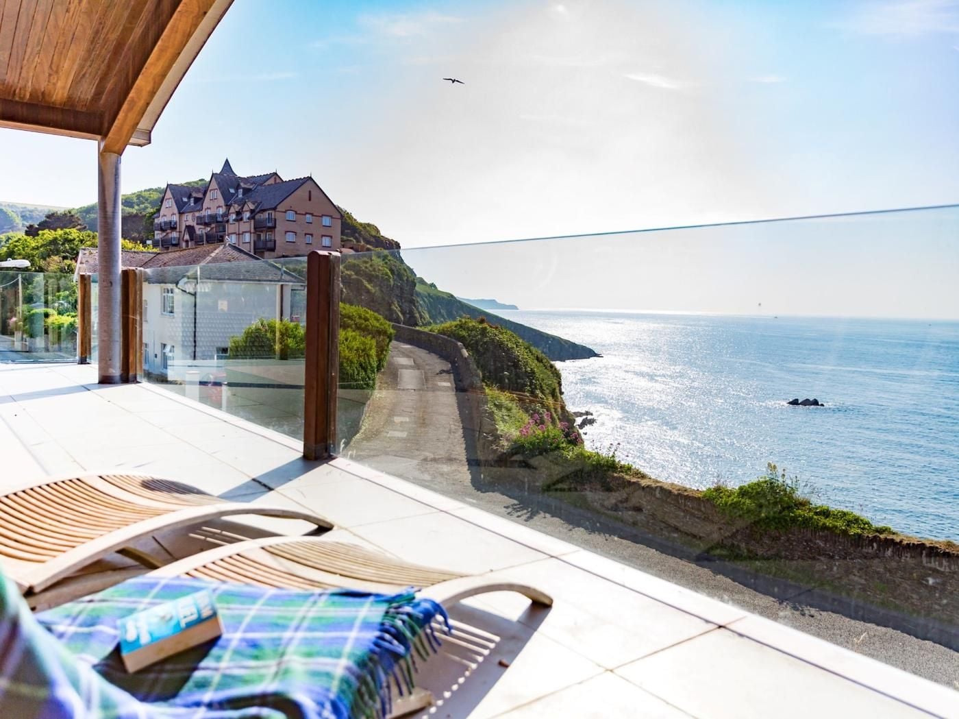A seaside terrace with a view of the ocean, a building in the background, and a chair with a blanket.