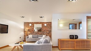 Een moderne woonkamer met een grijze bank, een houten dressoir, een bakstenen muur en een flatscreen televisie.