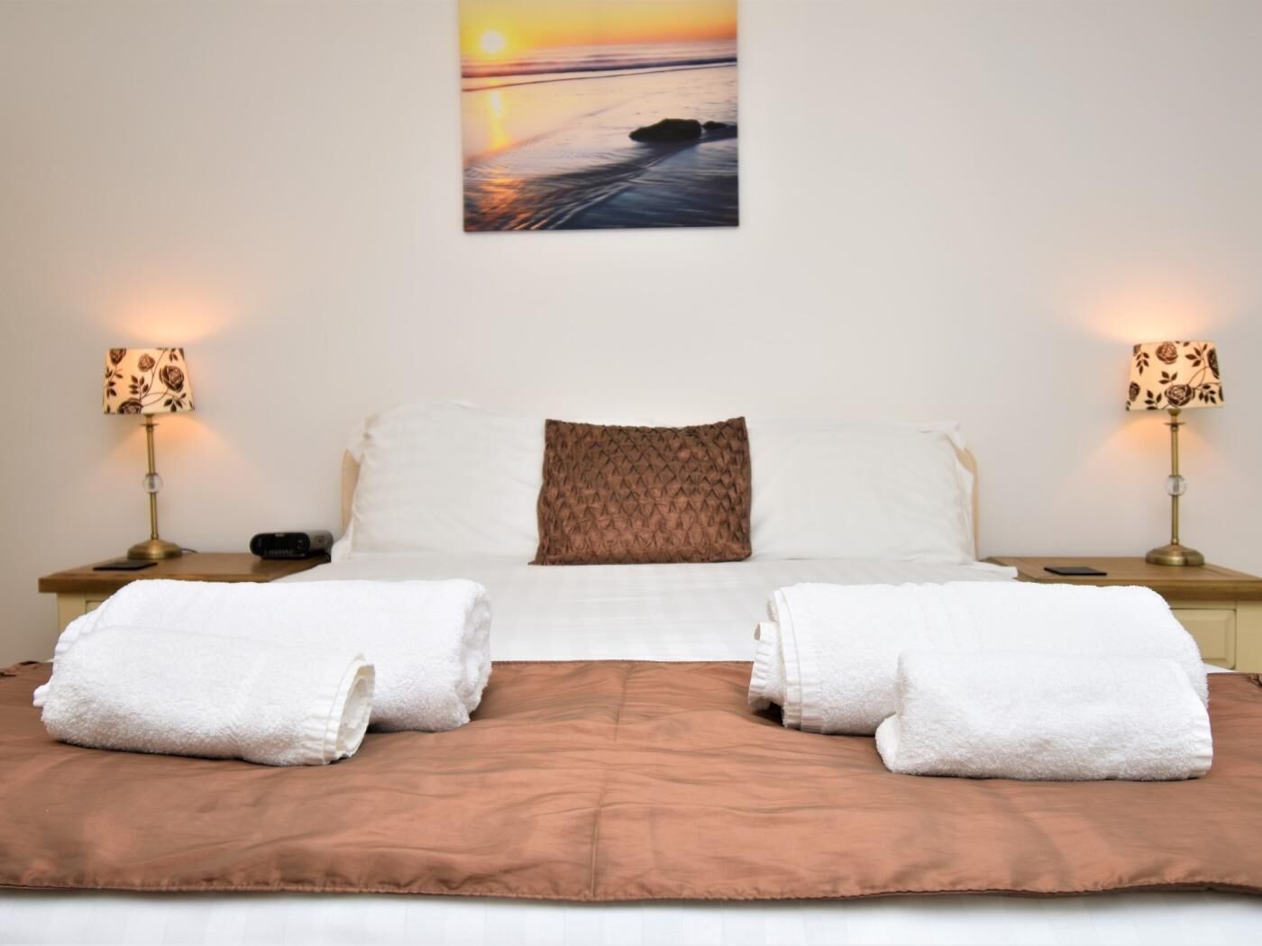 A neatly made bed with a brown blanket, two white towels, and a patterned pillow.