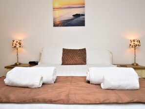 A neatly made bed with a brown blanket, two white towels, and a patterned pillow. - 1 Bed in Ilfracombe (oc-90074) (Ilfracombe)