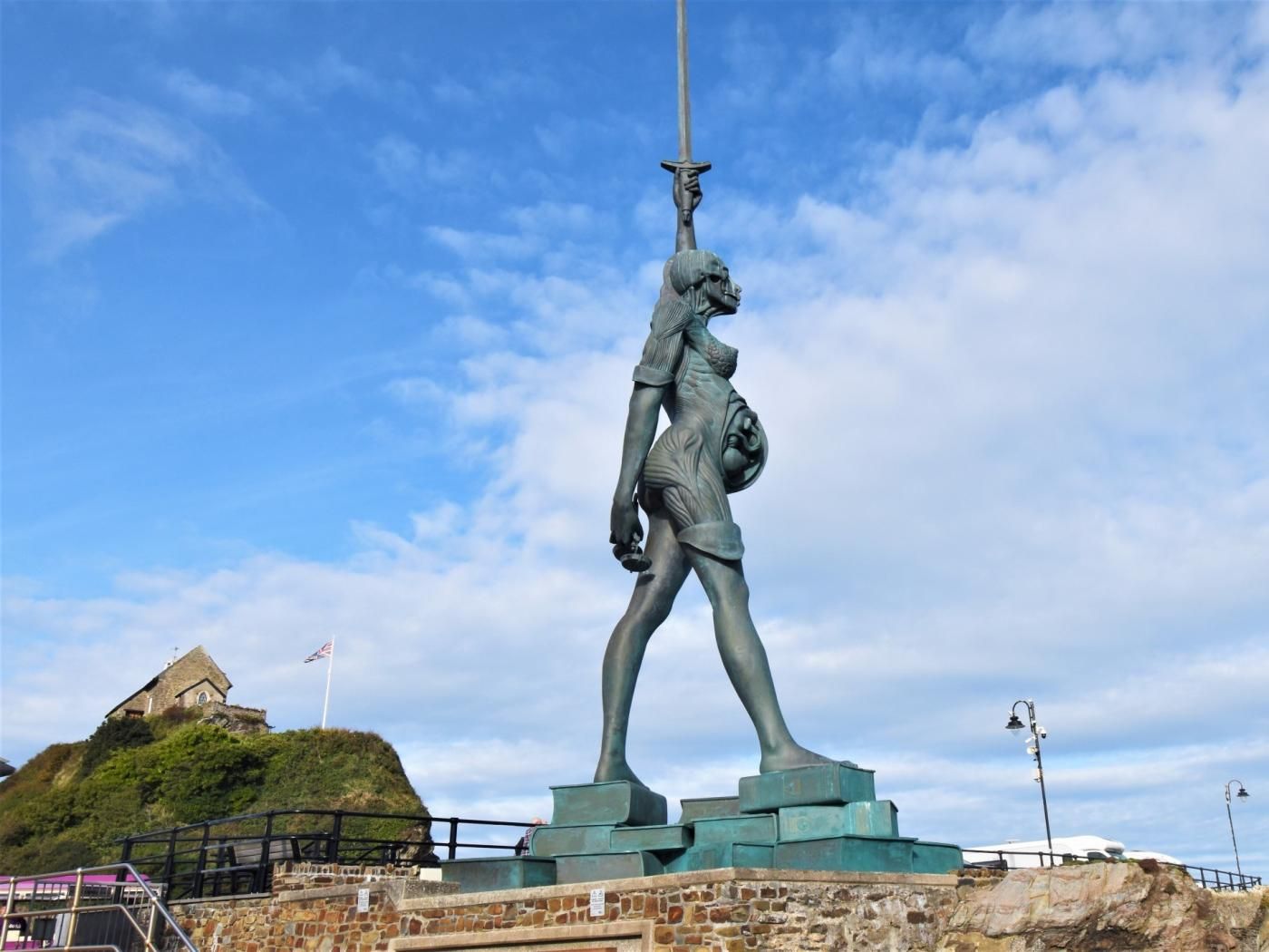 A statue of a figure holding a sword, set on a stone pedestal with steps leading up to it.