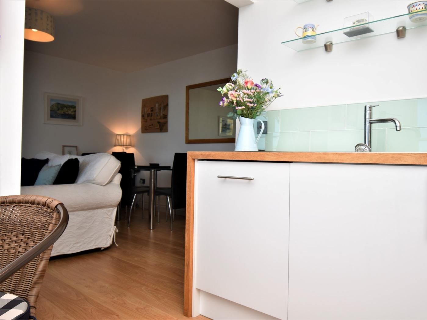 Une cuisine compacte avec un plan de travail blanc, un évier et un vase rempli de fleurs. On aperçoit à l’arrière un coin repas avec une table et des chaises.