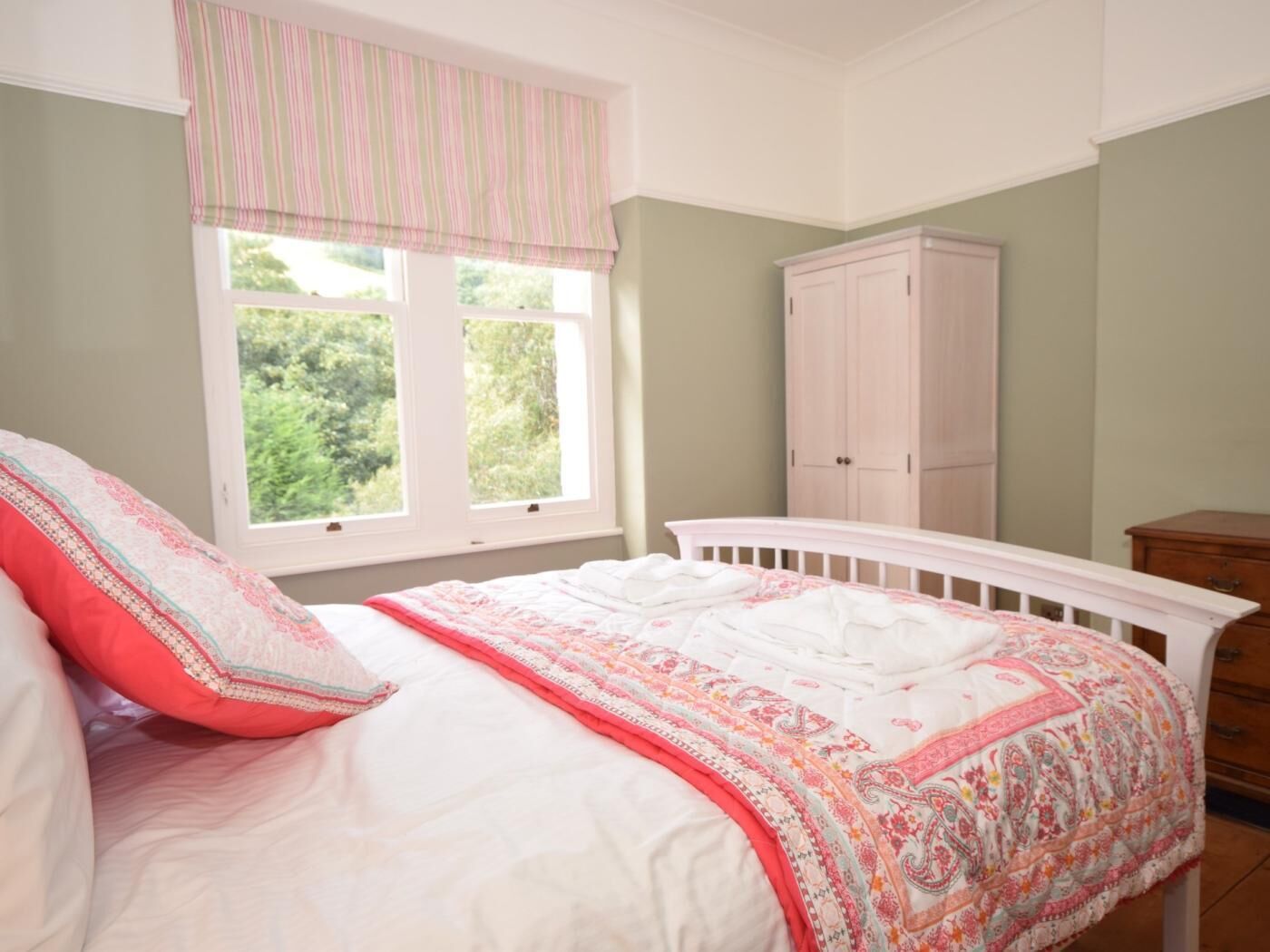 Une chambre à coucher avec un lit, une fenêtre avec des rideaux, une armoire et une commode.