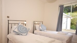 A bedroom with two beds, each with a headboard and a bedside lamp. - 6 Bed in Ilfracombe (oc-52585) (Combe Martin)