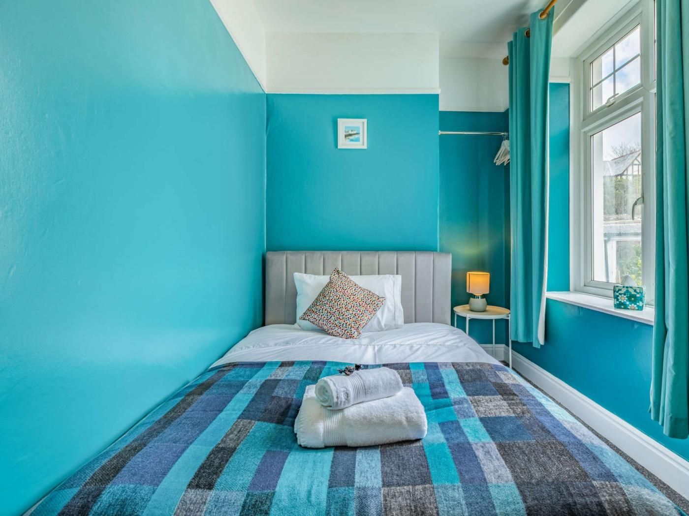 A bedroom with a bed, a nightstand, a window with curtains, and a wall-mounted picture.