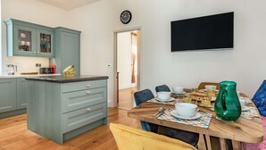 Eine moderne Küche mit einer zentralen Kochinsel, einem Essbereich mit Holztisch und einem an der Wand montierten Flachbildfernseher.