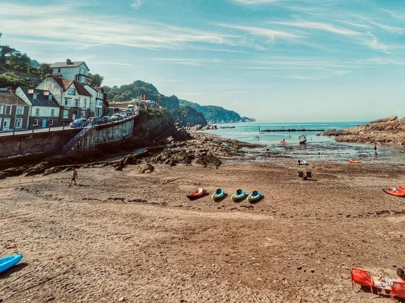Una platja costanera amb una filera de cases, una línia de roca i diverses canoes i un cànoi.