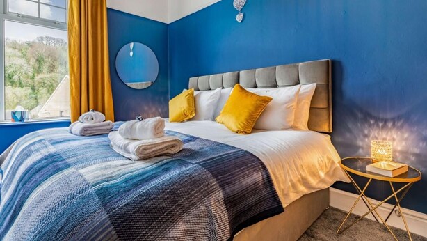 Ein Schlafzimmer mit einem Bett, einem runden Spiegel, einem Nachttisch mit Lampe und Blick ins Freie.