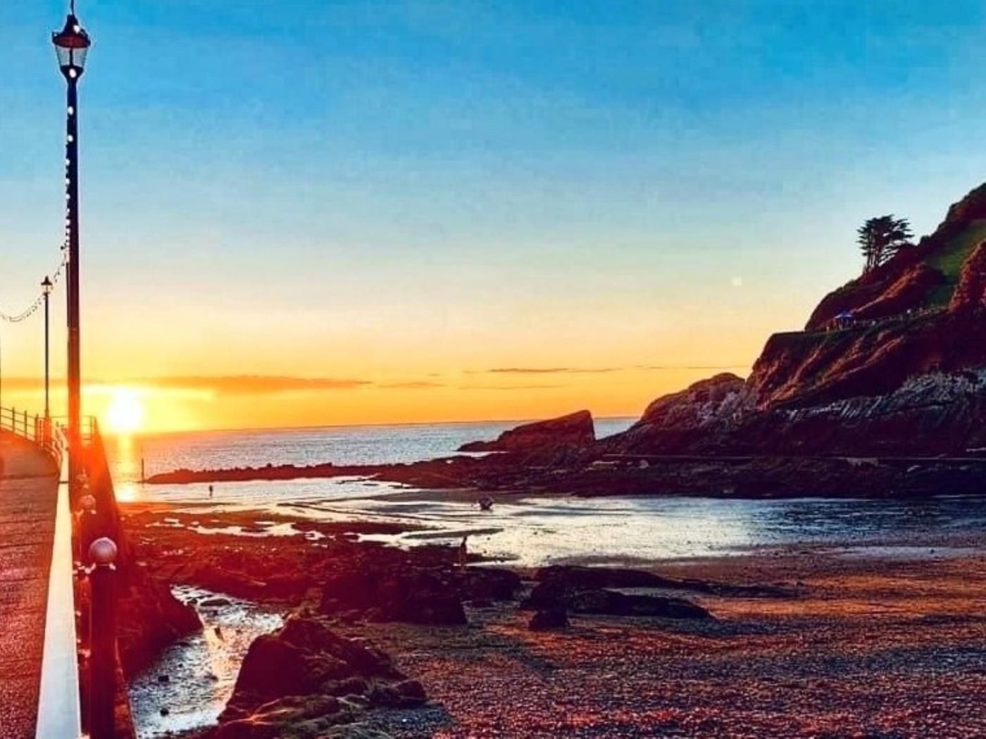 Un paysage côtier avec un phare, une côte rocheuse et un coucher de soleil.
