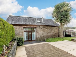 A stone building with a wooden deck, a glass door entrance, and a palm tree. - 3 Bed in Ilfracombe (oc-47348) (Berrynarbor)