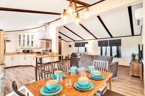 A spacious kitchen with white cabinets, a dining area with a wooden table set for four, and a living area with a sofa and a large window.