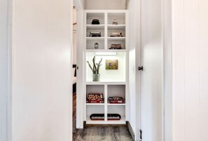 A narrow hallway with a white shelving unit containing books, decorative items, and a keyboard. - Hi View House - Desert Lookout with Fire Pit (Joshua Tree)