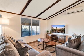 A modern living room with a sofa, a coffee table, a TV, and a large window. - Hi View House - Desert Lookout with Fire Pit (Joshua Tree)