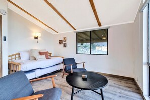 A modern room with a bed, two chairs, a small table, and a large window. - Hi View House - Desert Lookout with Fire Pit (Joshua Tree)