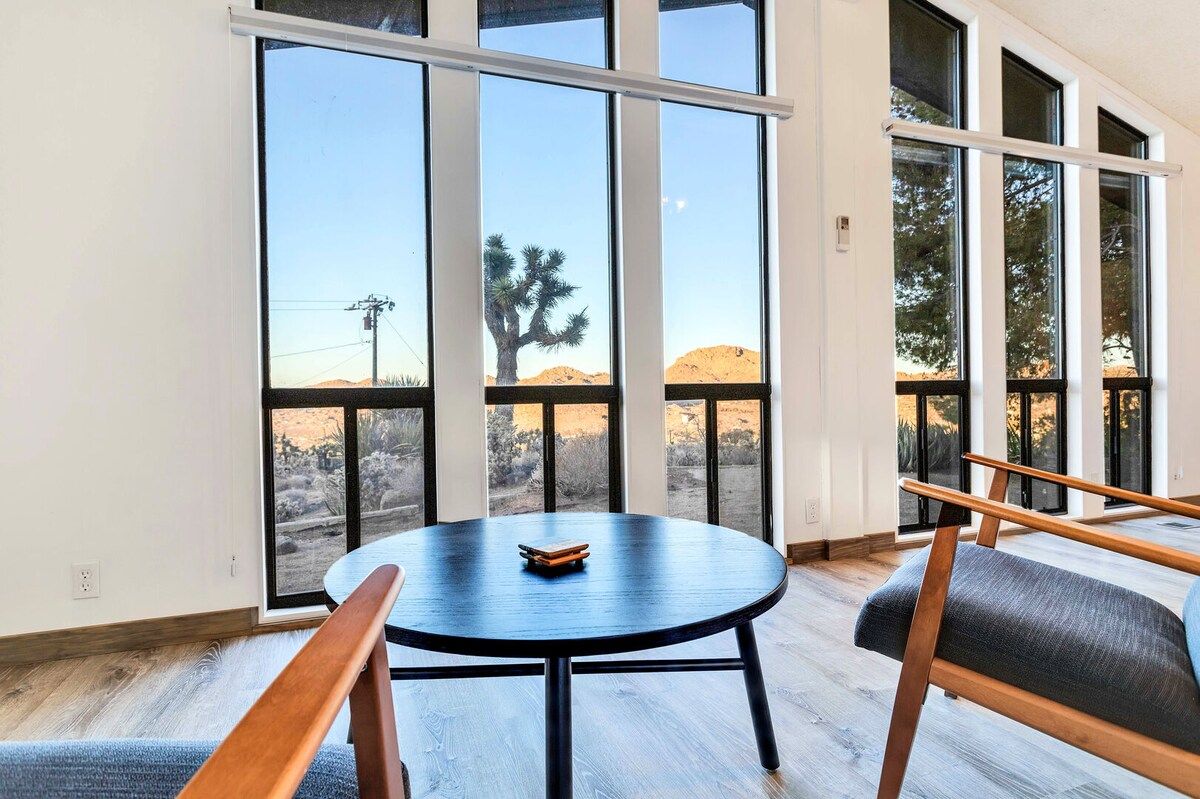 A room with a round table and benches, large windows with a view of a desert landscape.