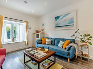 Ein Wohnzimmer mit einem blauen Sofa, einem Couchtisch mit Büchern, einem Fenster mit Vorhängen und einem Gemälde an der Wand.