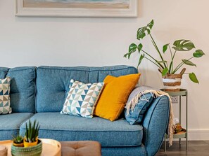 A blue sofa with patterned cushions, a small side table with a potted plant, and a framed picture on the wall. - 1 Bed in Kidderminster (oc-94769) (Oreton)