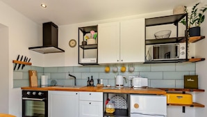 Eine kompakte Küche mit weißen Schränken, einer Holz Arbeitsplatte, einem eingebauten Backofen, einer Mikrowelle und einem Kühlschrank.