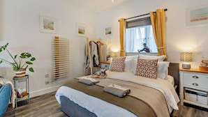 Ein ordentlich eingerichtetes Schlafzimmer mit Bett, Nachttischen, einem Sessel, einem Fenster mit Vorhängen und Wandbildern.
