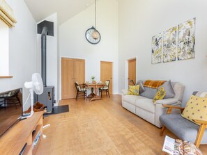 Ein geräumiger Wohnbereich mit Holzboden, einem Esstisch mit Stühlen, einer Couch mit Kissen und einer an der Wand befestigten Uhr.
