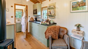 A cozy kitchen with wooden beams, a stove, and a dining area with a chair and table. - 1 Bed in Tewkesbury (oc-94686) (Bushley)