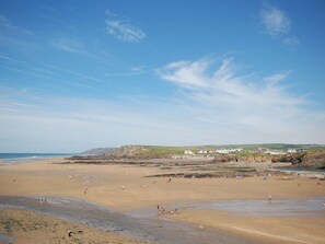 Ein weiter Sandstrand, bewölkter Himmel, ein Felsen und ein Dorf in der Ferne.