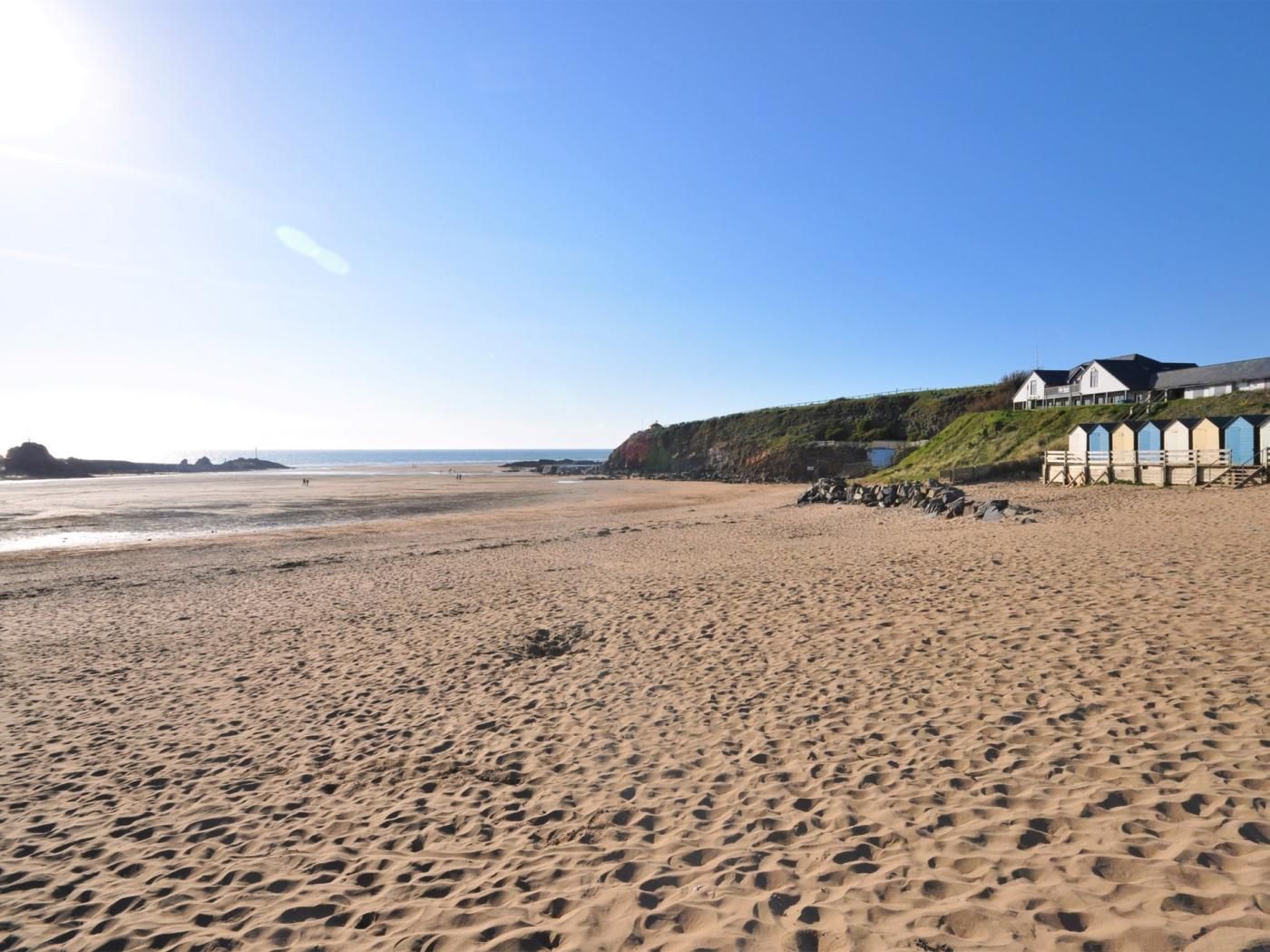 A sandy beach with a row of beach huts and a building with a sloped roof.
