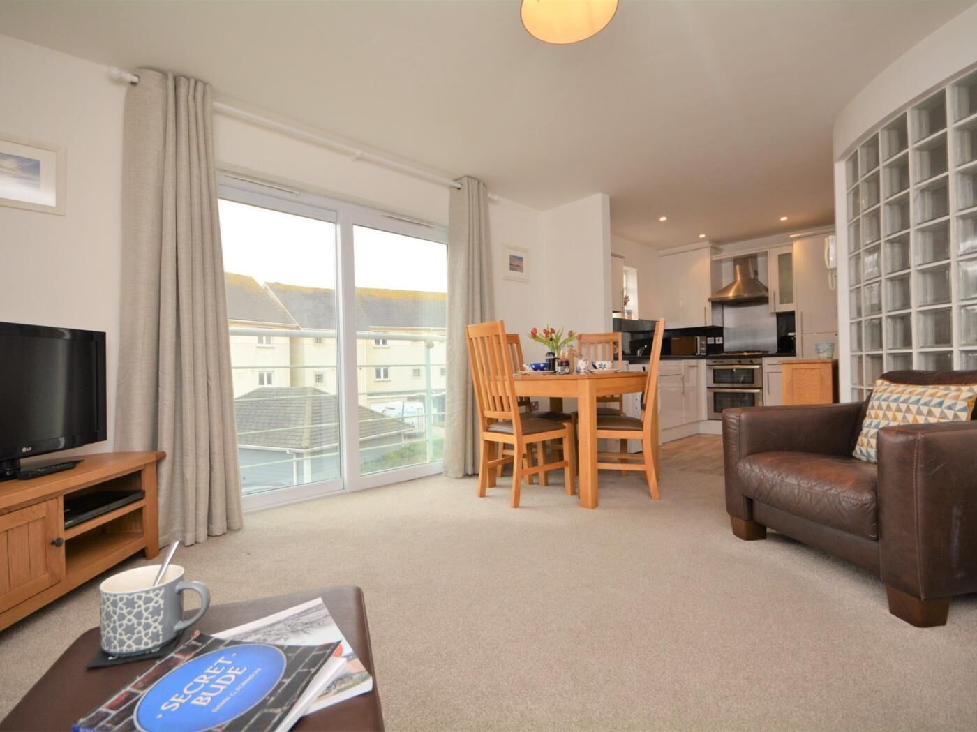A living room with a TV, a dining table with chairs, a sofa, and a kitchen in the background.