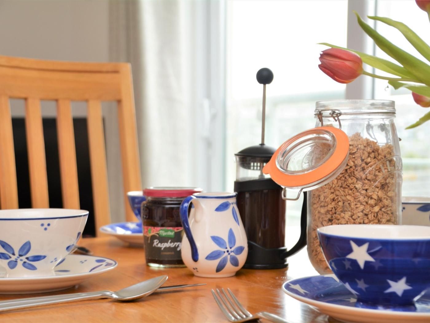Une table à manger avec une machine à café, un bocal de granola et un tulipe en arrière-plan.