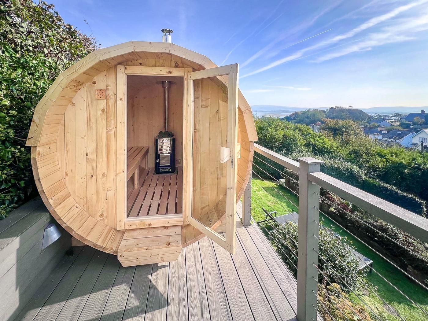 A wooden sauna structure with a door open, revealing a bench and a sauna heater inside.