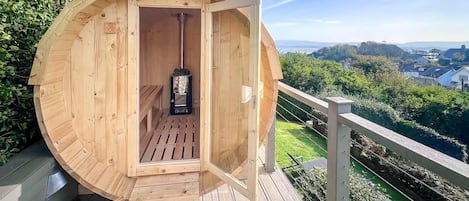 A wooden sauna structure with a door open, revealing a bench and a sauna heater inside.