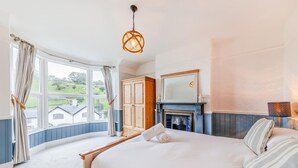A bedroom with a bed, a fireplace, a wardrobe, and a large window with curtains. - 7 Bed in Aberdyfi (oc-dy030) (Aberdovey)