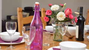 Une table à manger avec une bouteille violette, un vase rempli de fleurs, des verres à vin et une bouteille de vin.