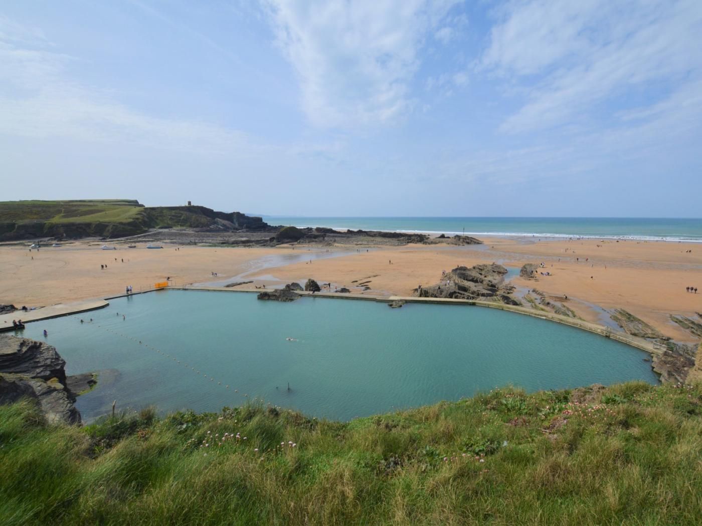 A coastal landscape with a beach, a rocky pool, and a grassy hill.