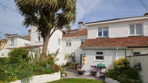 Une maison blanche avec un toit en tuiles, une pelouse et un jardin agrémenté de plantes et de fleurs.