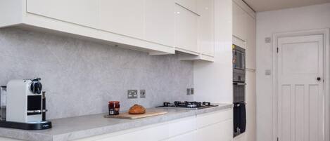 Una cocina moderna con armarios blancos, estufa integrada y una cafetera.