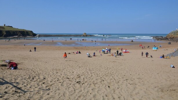 Une vaste plage de sable où l’on aperçoit des gens et des tentes, un ciel dégagé et, au loin, des falaises rocheuses.