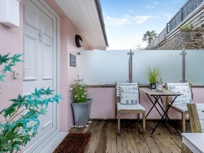 Eine Terrasse mit einem Holztisch und -stühlen, einem Blumentopf und einem kleinen Teppich.