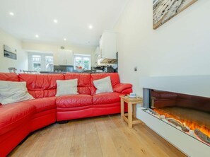 Ein rotes Ledersofa mit Kissen, ein kleiner Holztisch und ein Kamin mit Holzscheiten.