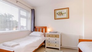 Ein Schlafzimmer mit einem Einzelbett, einem Schminktisch, einem Heizkörper und einem Fenster mit Jalousien.