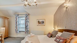 A bedroom with a bed, a wooden cabinet, a window with floral curtains, a radiator, and a wall-mounted light fixture. - 2 Bed in Keswick (oc-94995) (Keswick)