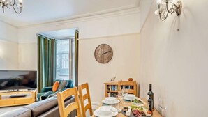 A dining area with a wooden table set for two, a television in the background, and a bookshelf. - 2 Bed in Keswick (oc-94995) (Keswick)