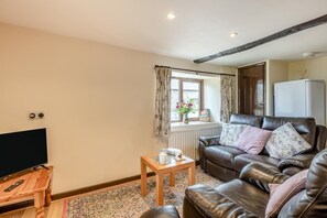 A living room with a leather sofa, a wooden coffee table, a television, and a window with curtains. - 2 Bed in Woolacombe (oc-43279) (Woolacombe)