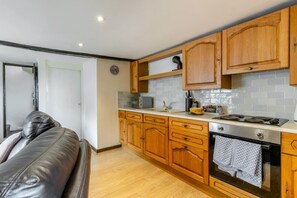 A compact kitchen with wooden cabinets, a microwave, a stove, and a tiled backsplash. - 2 Bed in Woolacombe (oc-43279) (Woolacombe)