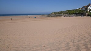 A wide sandy beach with a clear sky, a few people, and a building with a steep roof on the right. - 2 Bed in Woolacombe (oc-43279) (Woolacombe)